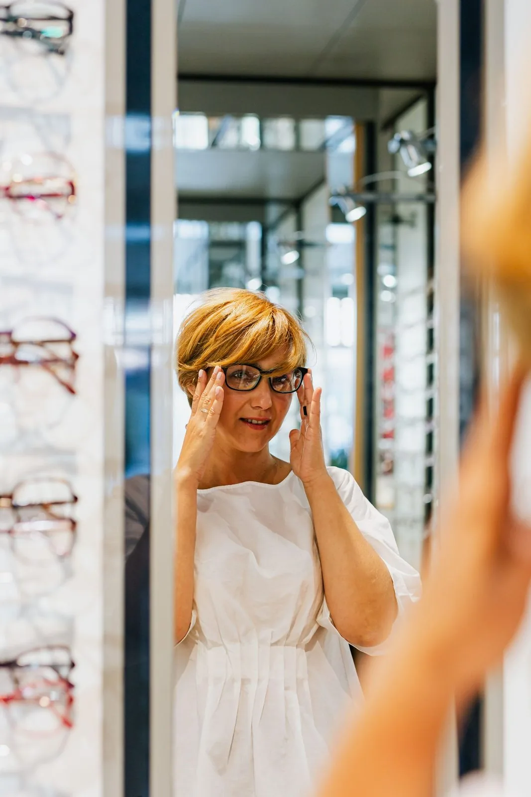 Cliente essayant une monture de vue devant le mur de lunettes