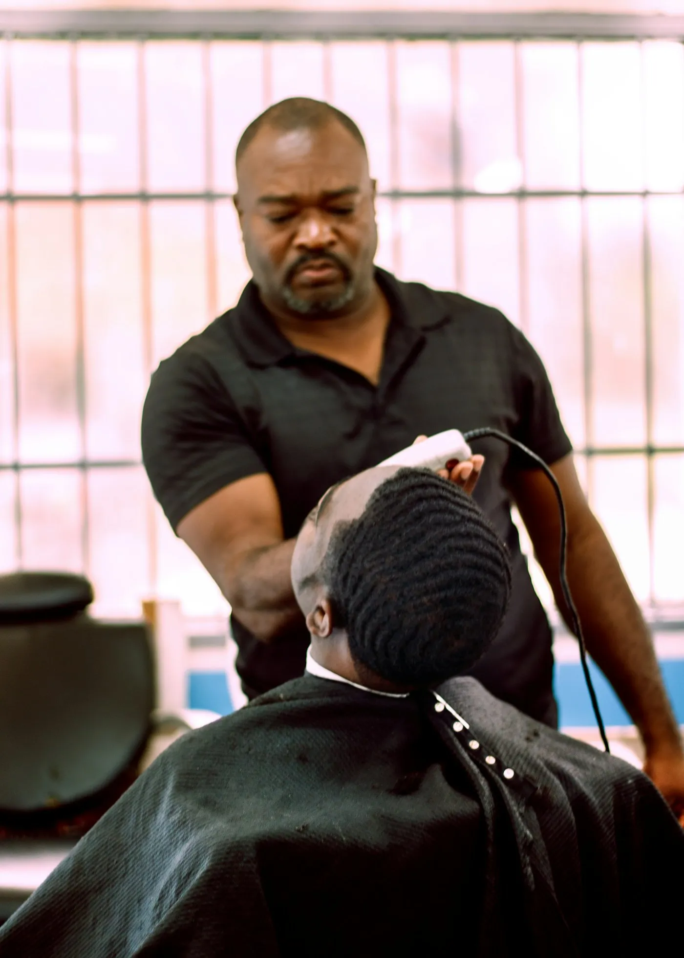 Le barbier, crâne rasé, passe la tondeuse sur la nuque d’un client